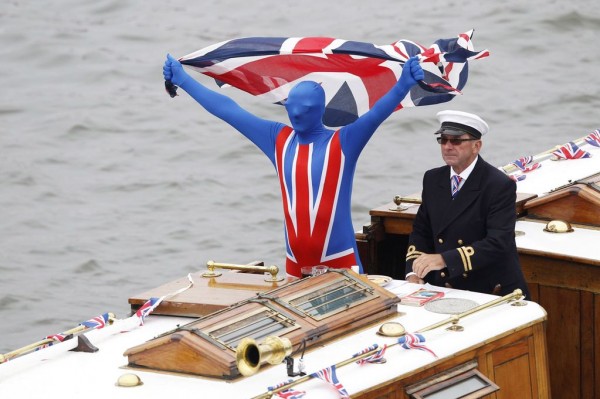 A+skipper+steers+a+boat+as+a+passenger+holds+up+a+Union+Flag+as+they+take+part+in+Queen+Elizabeth's+Diamond+Jubilee+pageant